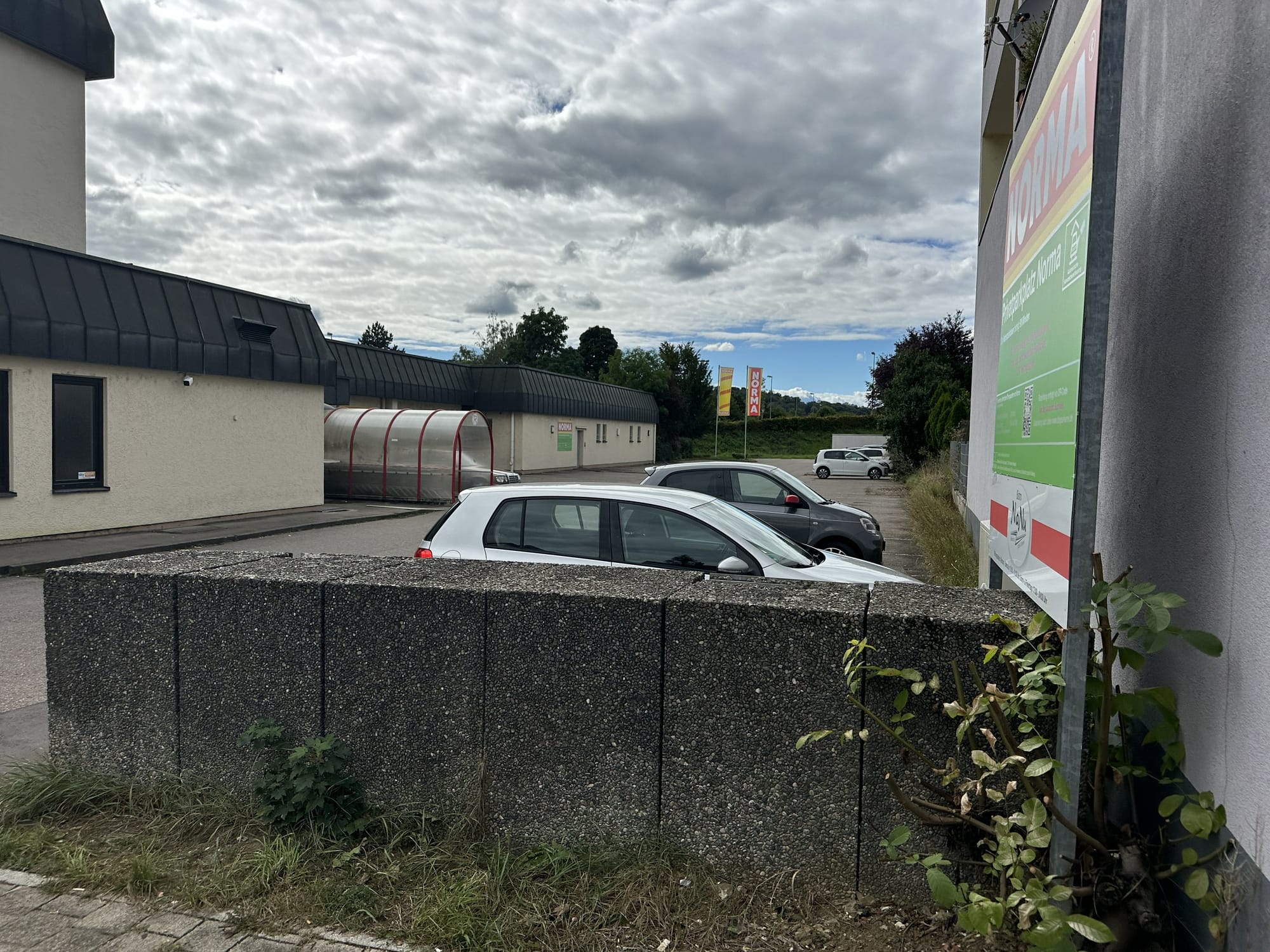 Norma-Filiale mit Kundenparkplatz, davor parkende Autos und die kombinierte Beschilderung von Norma und der Parkerei